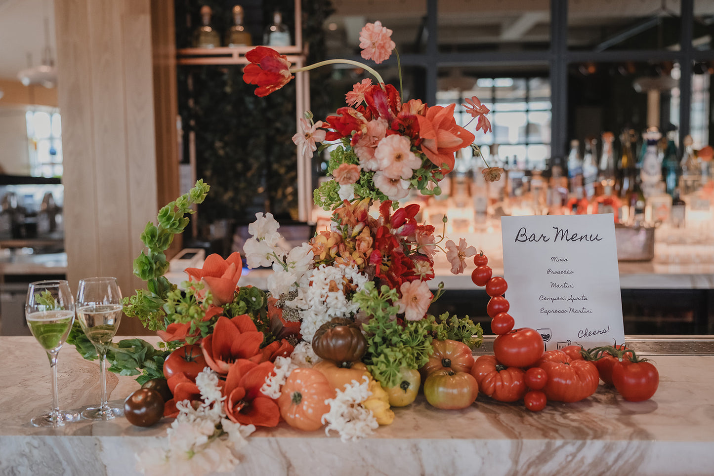 Botanical sculpture on a bar-top with hand-wired florals and tomatoes, highlighting a bar menu card.